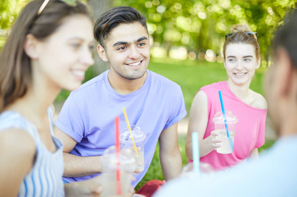 Щасливий хлопець і його друзі з напоями розмовляють на пікніку в природному середовищі
 - Фото, зображення