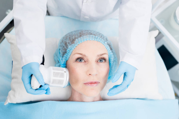 Donna matura godendo massaggio del suo viso con speciale dispositivo elettrico nel salone di bellezza
 - Foto, immagini