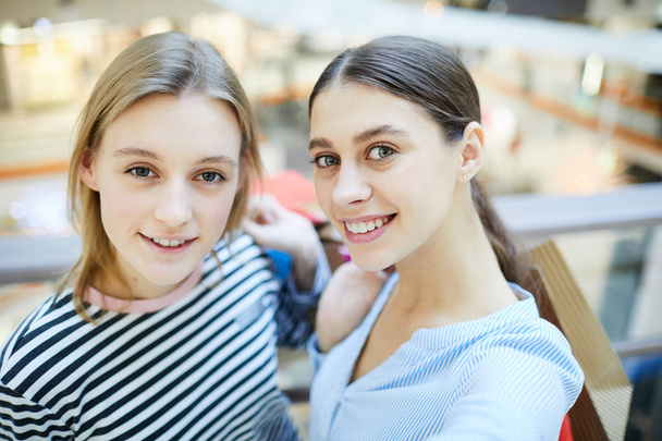 Two young cheerful shoppers standing in front of camera during seasonal sale in the mall - Фото, изображение
