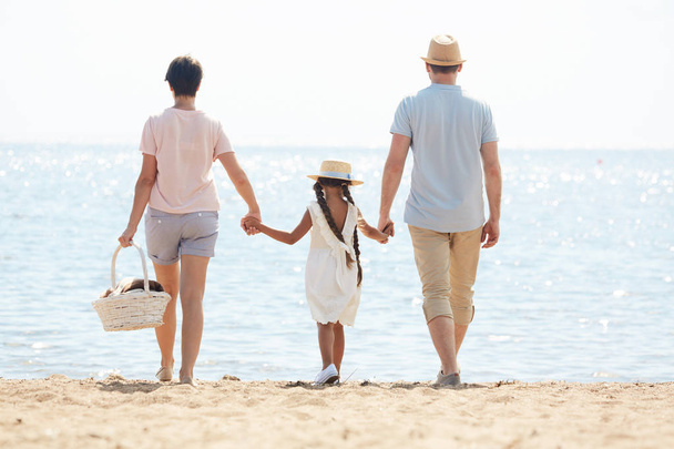 Família jovem de três vai fazer um piquenique à beira-mar no dia quente de verão ou durante as férias
 - Foto, Imagem