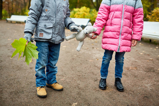 Dwa dzieci trzymanie łapy misia podczas spaceru w parku jesienią dnia lub weekendu - Zdjęcie, obraz