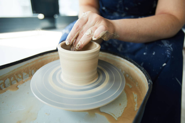 Handen van Potter tijdens het proces van het maken van klei potten en kannen op aardewerk wiel in workshop - Foto, afbeelding