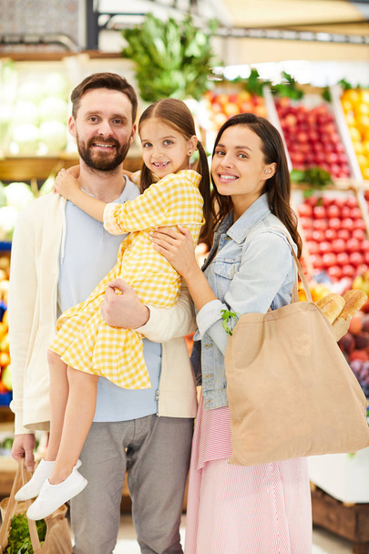 Optymistyczna młoda rodzina w casual Odzież stoi przed straganie żywności i patrząc na aparat, cieszą się zakupy razem w supermarkecie - Zdjęcie, obraz