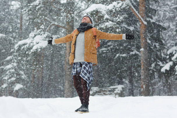 Libero giovane uomo con le braccia tese guardando verso l'alto mentre era eccitato per il tempo invernale, si trovava sotto la neve
 - Foto, immagini