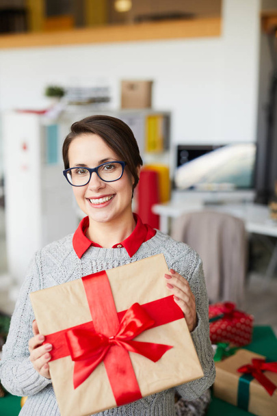 Молода усміхнена жінка з упакованою коробкою пов'язана з шовковою червоною стрічкою, що показує її вам
 - Фото, зображення
