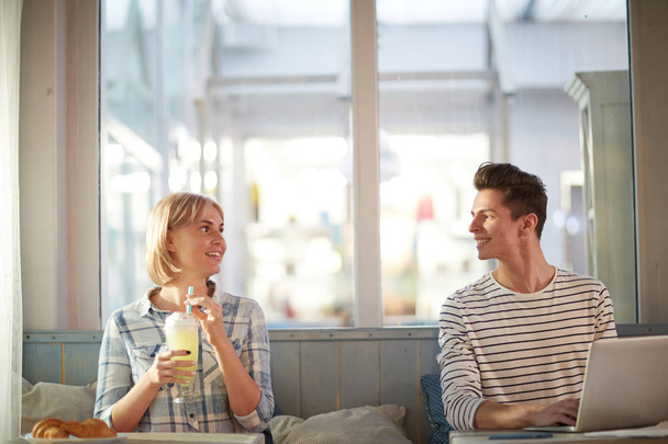 Gelukkige kerel met laptop en meisje met cocktail zittend in Café door naburige tafels en praten - Foto, afbeelding