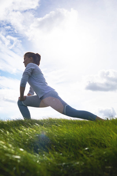 午前中に緑の芝生の上で運動しながら彼女の足を伸ばすアクティブな女性 - 写真・画像