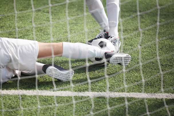 Legs of two footballers pursuing soccer ball during game on green field behind net - Foto, imagen