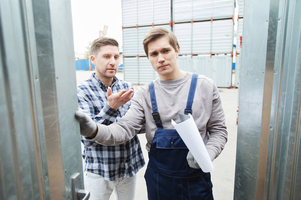Serious pensive man asking storage worker about capacity of container and gesturing while explaining what he wants to place inside - Valokuva, kuva