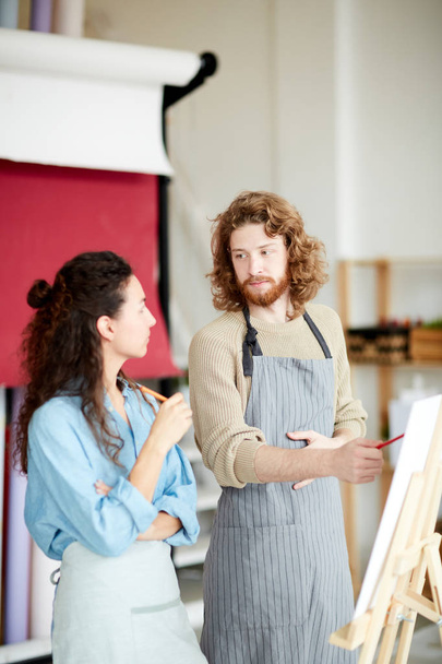 Jovem e mulher em roupas de trabalho em pé por cavaletes e discutindo ideias enquanto brainstorming
 - Foto, Imagem