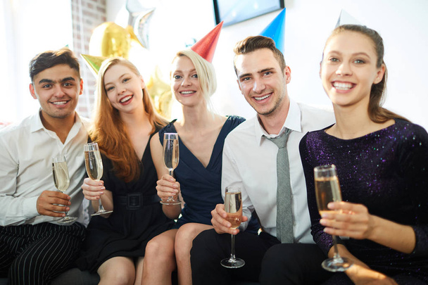 シャンパンのフルートを持ち、パーティーを楽しむエレガントな服装で5人の幸せな若者 - 写真・画像