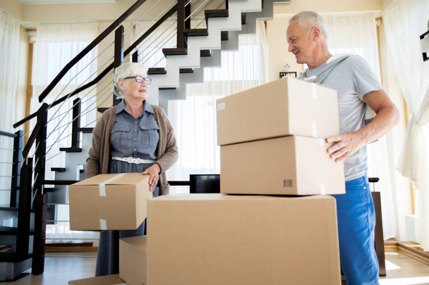Portrait of happy senior couple packing cardboard boxes while moving to new house - Photo, Image