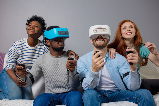 Two guys playing video games using VR glasses and girlfriends support them. - Fotó, kép