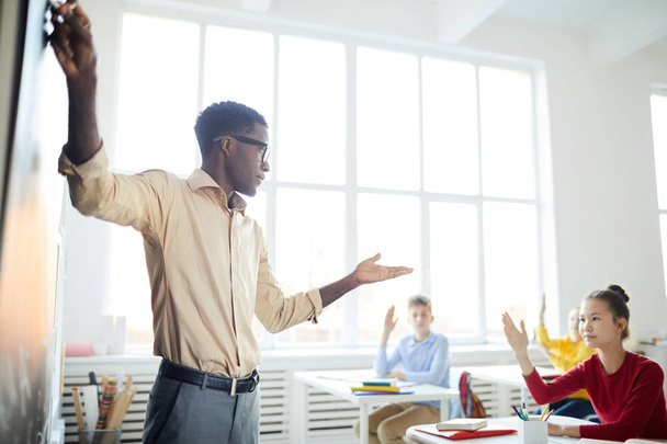 Věříme, že mladý afroamerický učitel míří na tabuli, zatímco v hodině hovoří se středoškoláky. - Fotografie, Obrázek