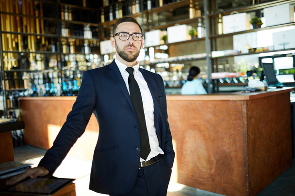 Серьезный бизнесмен в элегантном костюме смотрит на вас, стоя у входа в кафе
 - Фото, изображение