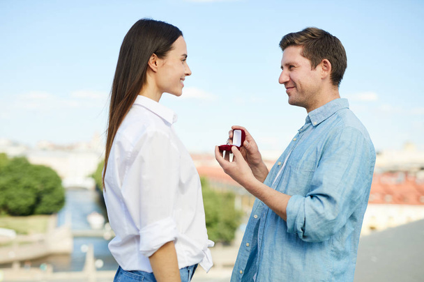 junger Mann mit Ring-Box steht vor seiner Freundin und macht ihr einen Heiratsantrag - Foto, Bild