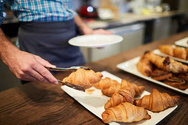 Serveur ou vendeur mettant un des croissants croustillants sur l'assiette pour le client du café
 - Photo, image
