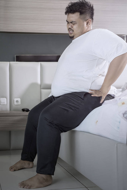 Young fat man having backache after waking up - Фото, изображение