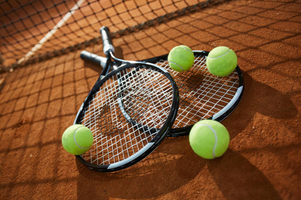 Deux nouvelles raquettes de tennis et quatre balles sur un terrain sablonneux avec filet sur fond
 - Photo, image
