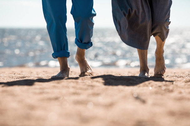 砂浜のビーチで晴れた日に散歩をする年配のカップルの裸の足 - 写真・画像
