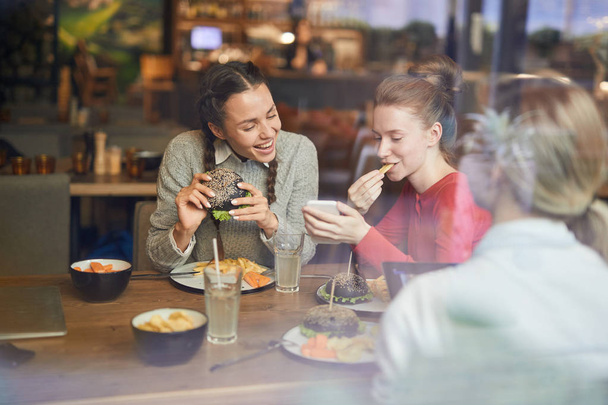 Cute girls making funny selfie by lunch while spending time in fast food cafe - Photo, Image