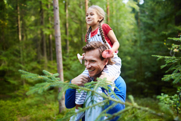 glückliches kleines Mädchen mit zwei Pilzen, die auf dem Hals ihres Vaters sitzen, während sie im Wald chillen - Foto, Bild