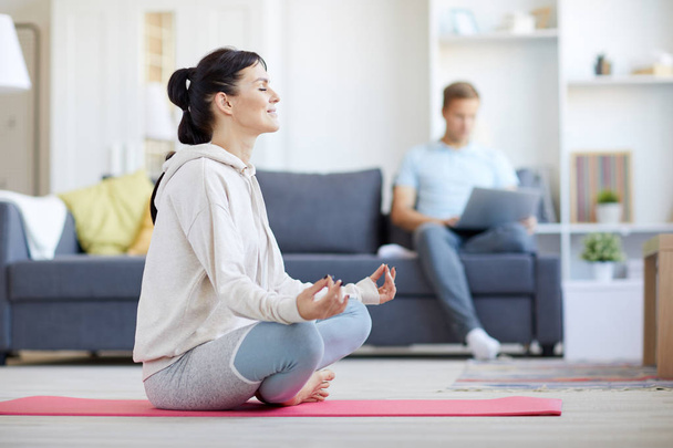 Nuori paljain jaloin nainen aktiivisissavaatteet meditointi aiheuttaa lootuksen lattialla kotona
 - Valokuva, kuva