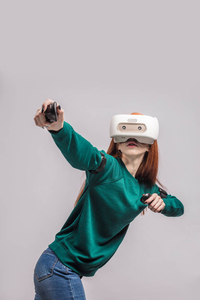 Confident redhead woman wearing virtual reality headset, aiming from the bow - Fotó, kép