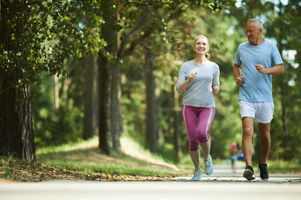 Active and healthy aged couple running in natural environment on summer morning - Photo, Image