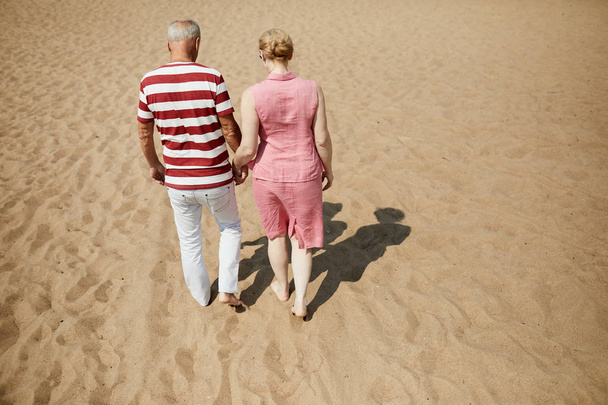 Milující starší dvojice v přesnotě pěšky po horkém letním dnu na písečné pláži - Fotografie, Obrázek