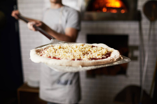 Fırına koymadan önce fırıncı tarafından tutulan çiğ pizza ile metalik maça veya tepsi - Fotoğraf, Görsel