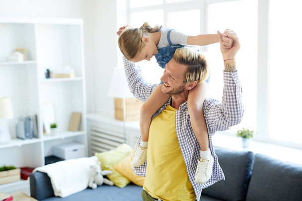 Homem alegre em casualwear desfrutando de brincar com sua adorável filha em casa
 - Foto, Imagem