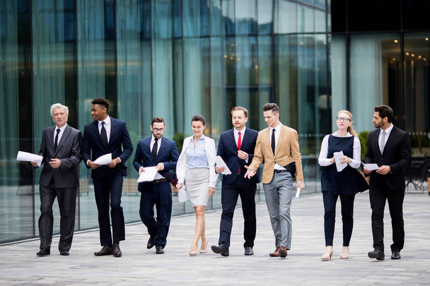 Several business people in elegant suits walking by modern building while having talk with each other - Foto, imagen