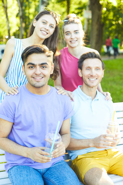 Rapazes felizes com bebidas e suas namoradas gostando de sair no parque no dia ensolarado
 - Foto, Imagem