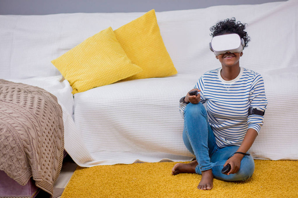 African woman watching video using VR glasses with remote control at home. - Foto, Bild