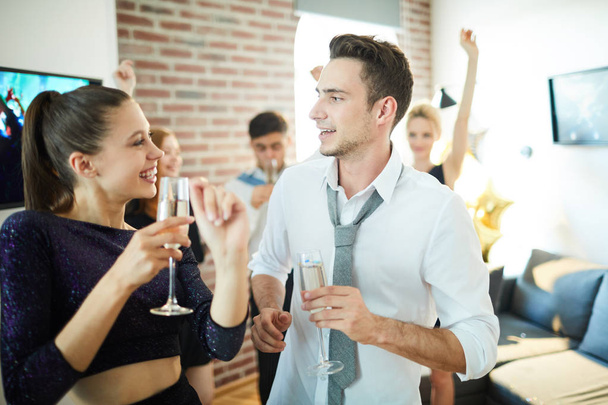 Счастливая молодая танцующая пара с флейтами шампанского разговаривает дома, собирая друзей
 - Фото, изображение