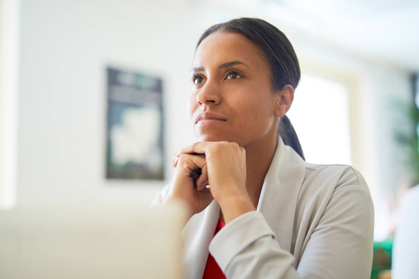 Young pensive mixed-race businesswoman keeping her hands under chin while thinking of something - Foto, Bild
