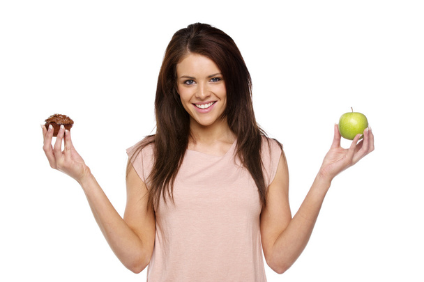 Brunette woman holding up an apple and cake - Foto, afbeelding