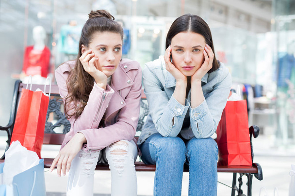 İki genç sıkılmış kadın alışveriş merkezinde alışveriş sonra bankta oturan gündelik giysiler - Fotoğraf, Görsel