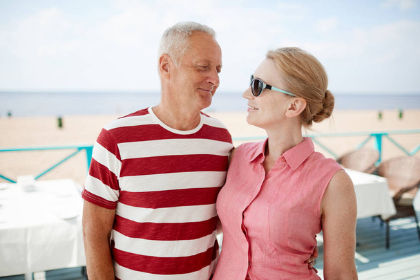 Felices cónyuges mayores mirándose en el resort de verano mientras pasan el día cerca de la playa
 - Foto, Imagen