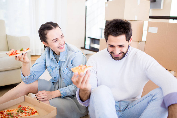 Jovem casal rindo se divertindo enquanto come pizza após a mudança para casa nova
 - Foto, Imagem