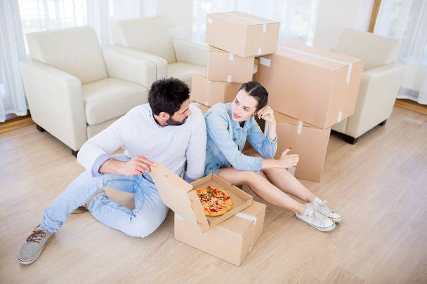 Genç çift yemek Pizza online hizmetten toplanmaz ve yeni evde katta otururken konuşmak zorunda - Fotoğraf, Görsel