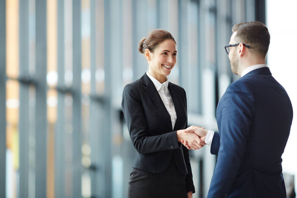 Young smiling businesswoman giving handshake to foreign business partner at meeting - Фото, изображение