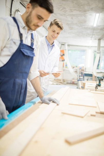 Молодой эксперт в белой одежде, стоящий рядом с инженером в рабочей одежде и заботящийся о рабочем процессе
 - Фото, изображение