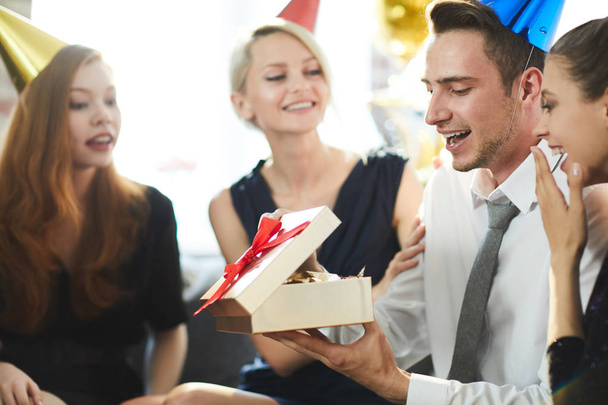 Счастливый молодой человек открывает коробку подарков и смотрит на подарок на день рождения от своих друзей
 - Фото, изображение