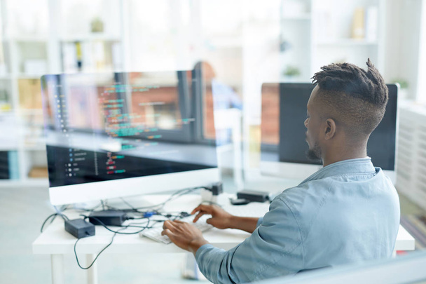 Visão traseira de jovens especialistas afro-americanos testando novos softwares enquanto se sentam no fornt do monitor de computador
 - Foto, Imagem