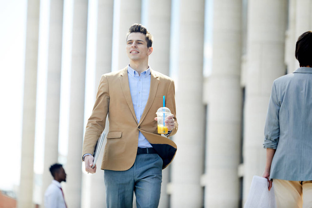junger Geschäftsmann in Formalbekleidung trinkt, während er sich im städtischen Umfeld bewegt - Foto, Bild