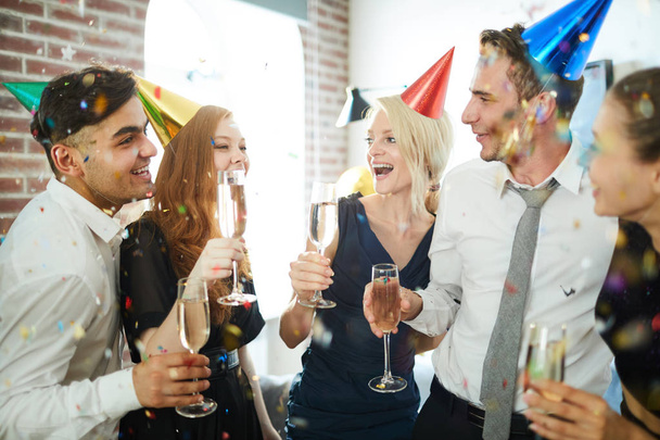 Amigos extáticos en gorras de cumpleaños disfrutando de fiesta y brindis con champán
 - Foto, imagen