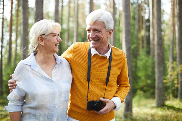Joyeux couple de personnes âgées affectueux se rafraîchissant dans la forêt le jour d'été, parlant et photographiant la nature
 - Photo, image