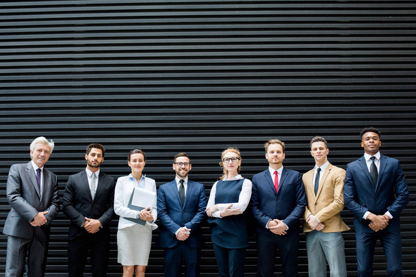 Reihe eleganter Delegierter in eleganter Formalbekleidung vor dunkelgrauem Hintergrund - Foto, Bild